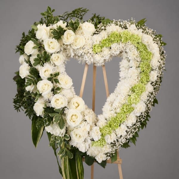 Heart-shaped white floral wreath on a wooden easel with green accents