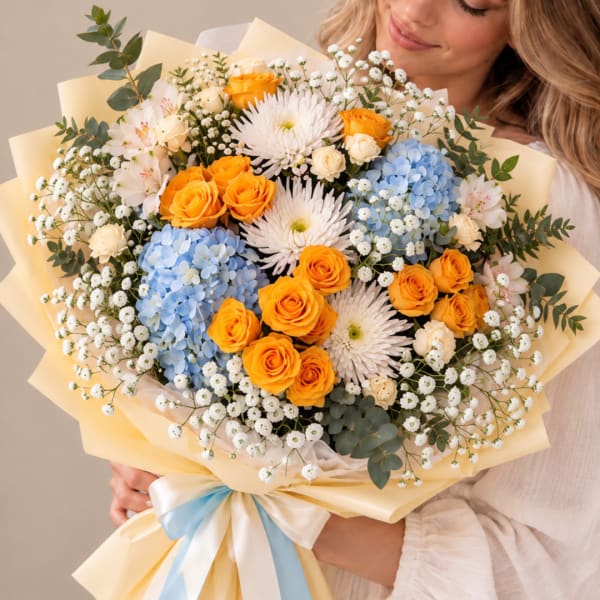 Bouquet of orange roses, blue hydrangeas, and white daisies wrapped in pale paper
