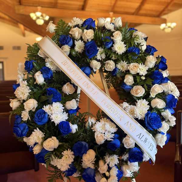 Blue and white floral funeral wreath with a memorial ribbon on an easel