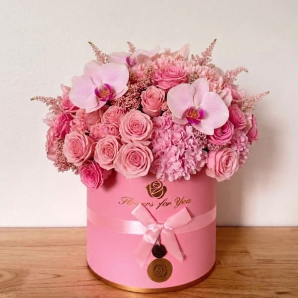 Pink roses and orchids arranged in a round pink box with a ribbon