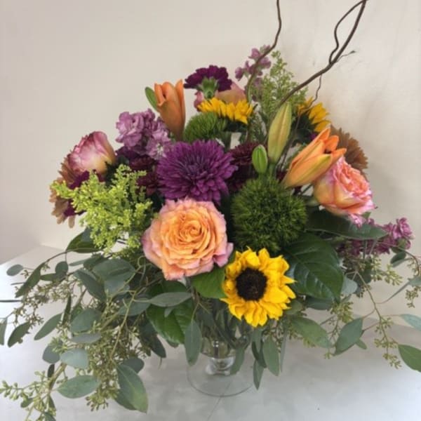 Mixed bouquet of purple, peach, and yellow flowers in a clear vase