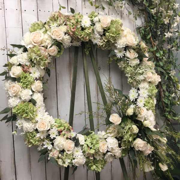 Large floral wreath with white and pale green flowers on a wooden backdrop