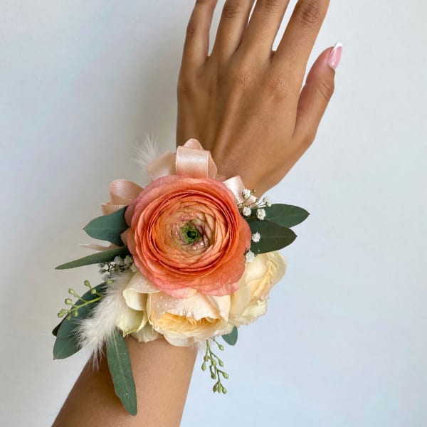 Peach and cream wrist corsage with ribbon and greenery on a hand