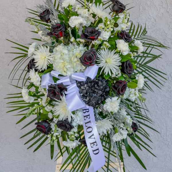 Standing funeral wreath of white flowers and dark roses with a ribbon