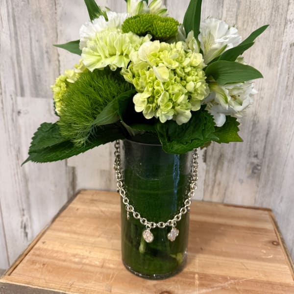 Green and white floral arrangement in a tall glass vase with a chain accent