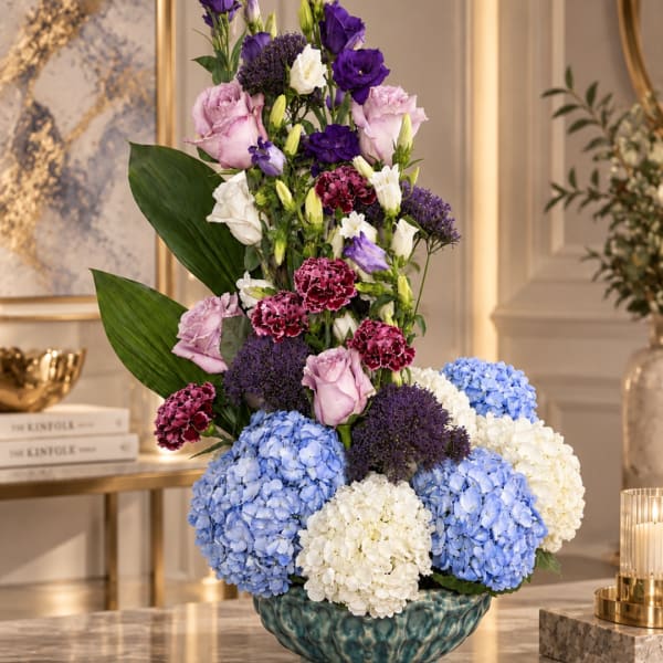 Tall floral arrangement with purple, pink, white, and blue blooms in a teal vase