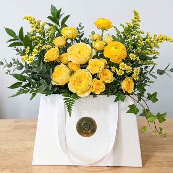 Yellow roses and small yellow filler flowers in a white gift bag