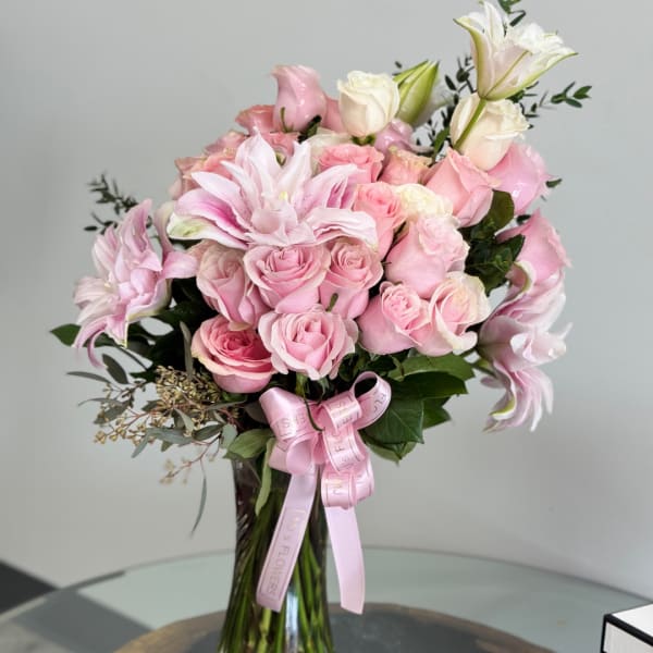 Pink roses and lilies arranged in a tall glass vase with a pink ribbon