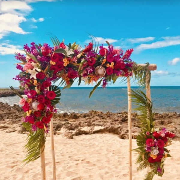 Floral arch with red, pink, and white flowers on a beach