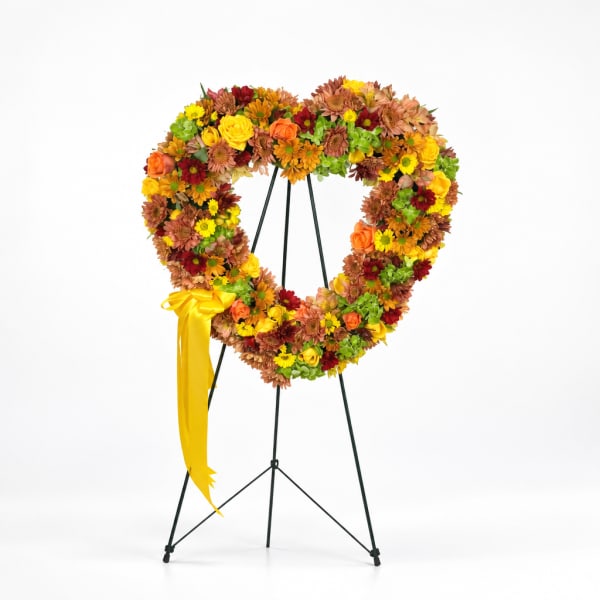 Heart-shaped floral wreath on a stand with a yellow ribbon
