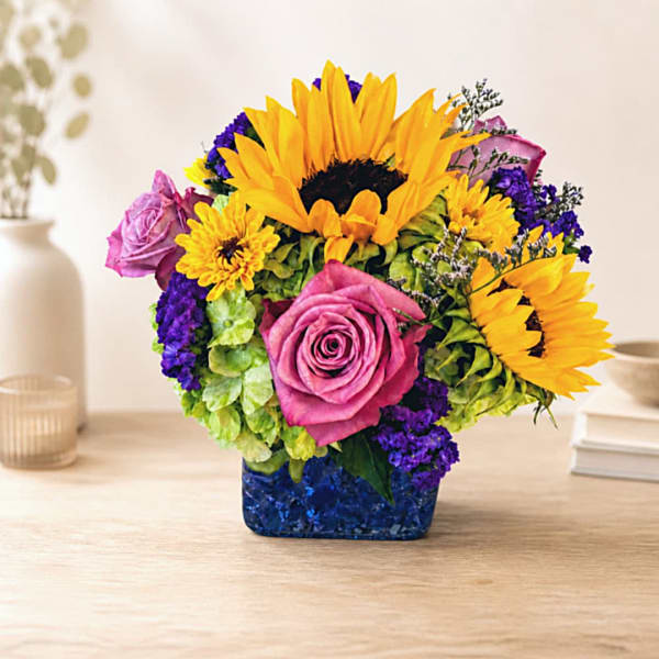 Colorful bouquet with sunflowers, pink roses, and purple flowers in a blue vase