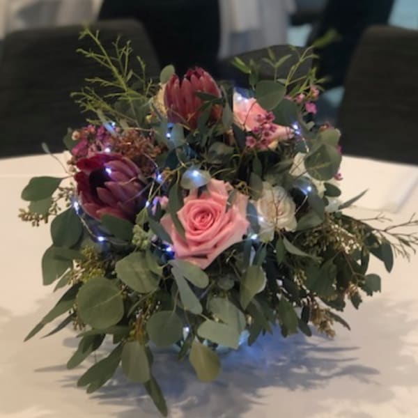 Pink and burgundy flowers arranged with greenery and small lights