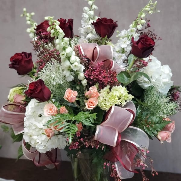 Bouquet of burgundy and blush roses with white blooms in a glass vase