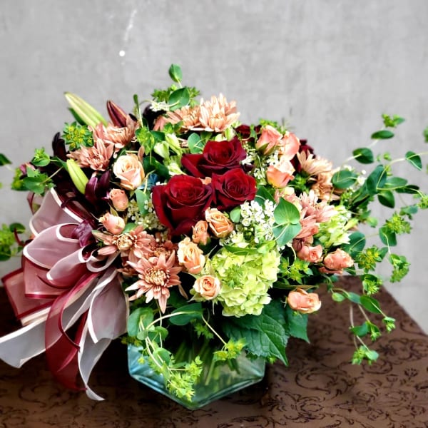 Mixed bouquet of red roses, peach spray roses, and pink mums in a glass vase
