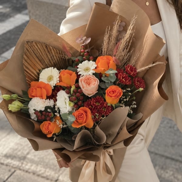 Handheld bouquet of orange and white flowers wrapped in brown paper