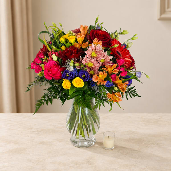 Colorful mixed bouquet in a clear glass vase with a small candle nearby