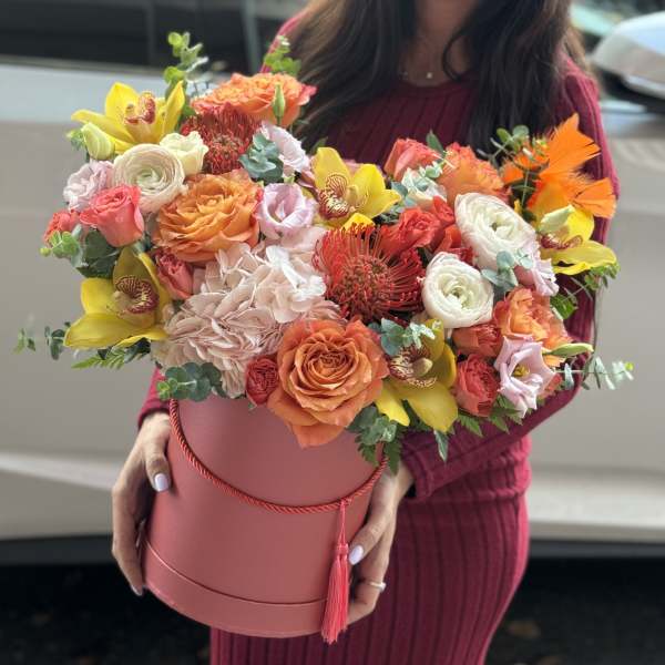 Large mixed bouquet in a pink hatbox with orange, yellow, and white blooms