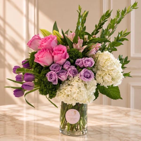 Pink roses, purple tulips, white hydrangeas, and lavender roses in a glass vase
