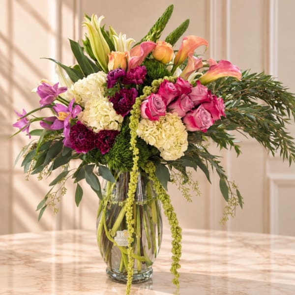 Mixed bouquet of pink roses, lilies, hydrangeas, and calla lilies in a glass vase