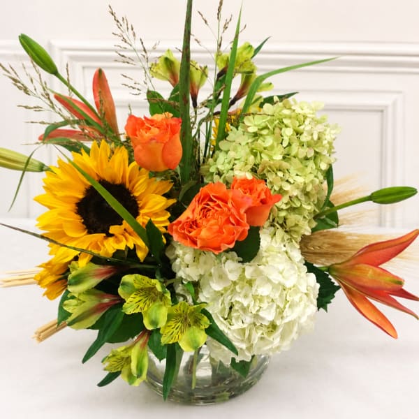 Bouquet of sunflowers, orange roses, and white hydrangeas in a glass vase