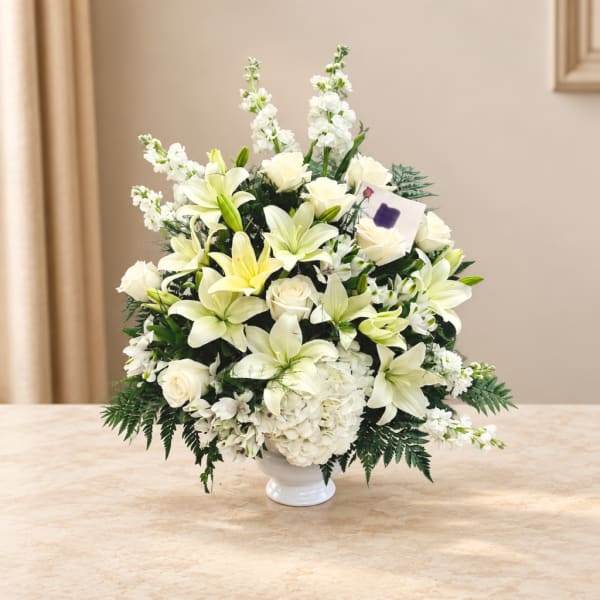 White lilies and roses arranged in a white vase with white filler flowers