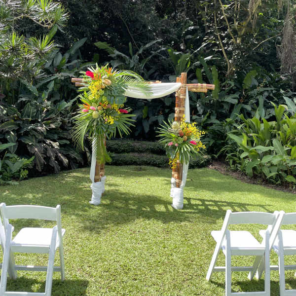 Tropical floral arch with white drape in a garden setting