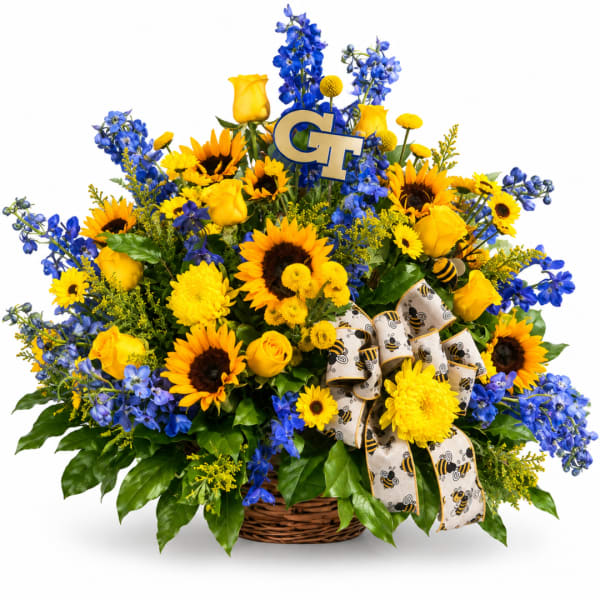 Basket arrangement of yellow roses, sunflowers, and blue flowers with a bee ribbon