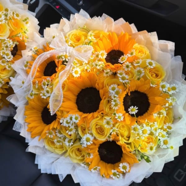 Bouquet of sunflowers, yellow roses, and small white daisies wrapped in white paper