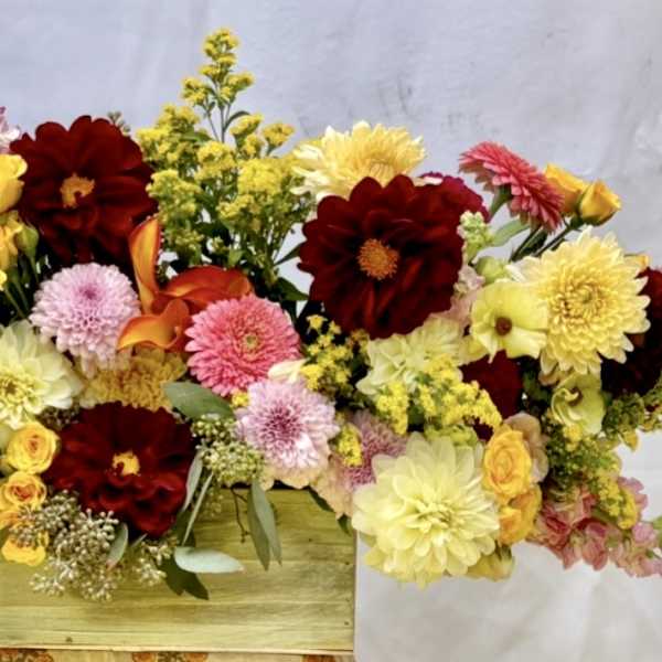 Mixed bouquet of red, pink, and yellow flowers in a wooden box