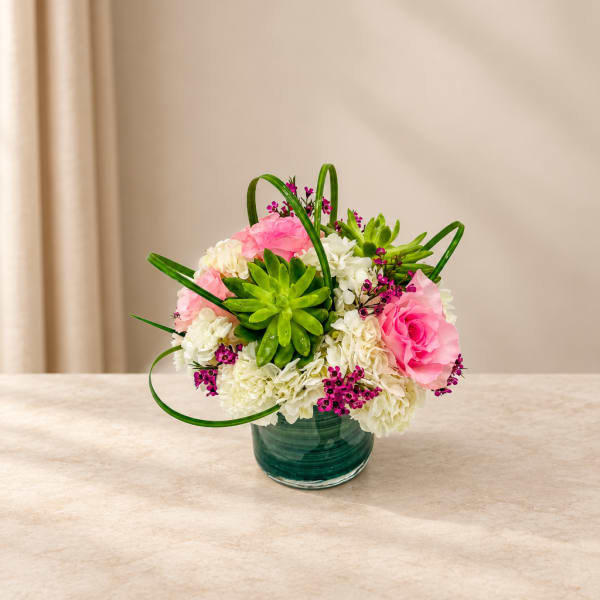 Pink and white flower arrangement in a green glass vase