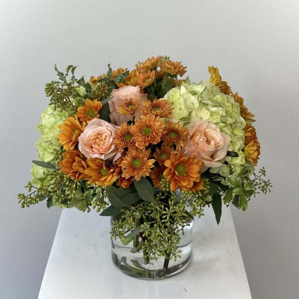 Orange and blush flowers in a clear glass vase with pale green hydrangeas