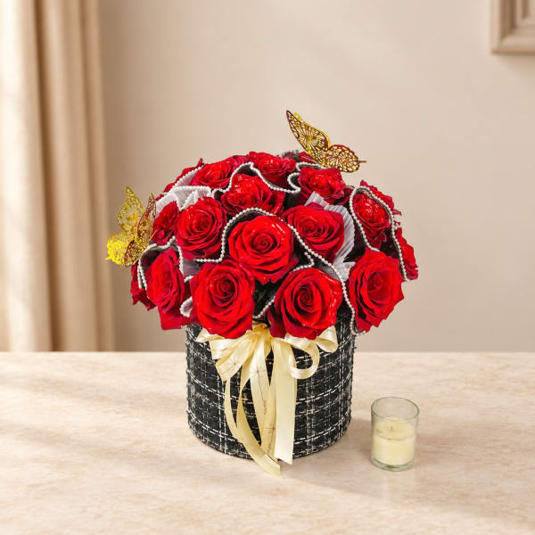 Red roses arranged in a black round box with a ribbon and butterfly accents