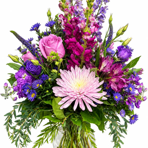 Mixed bouquet of pink, purple, and blue flowers in a clear glass vase