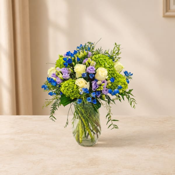 Bouquet of blue, lavender, and cream flowers in a glass vase