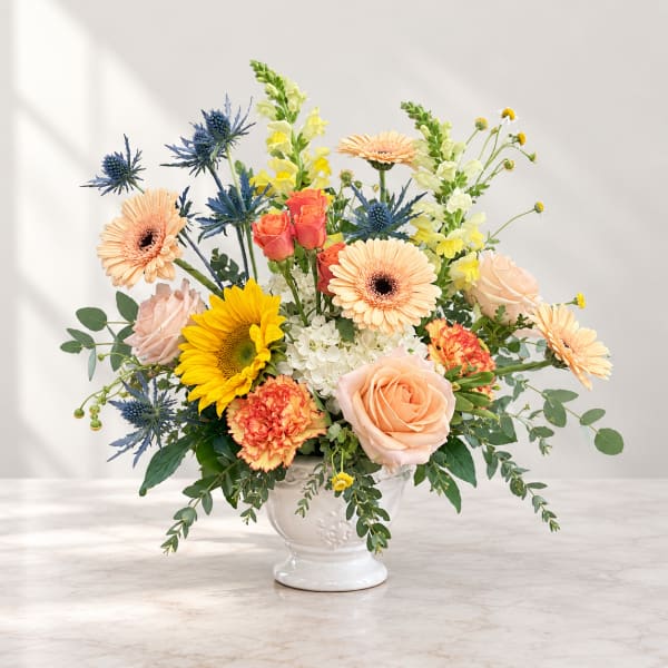 Mixed bouquet of peach, yellow, and blue flowers in a white vase