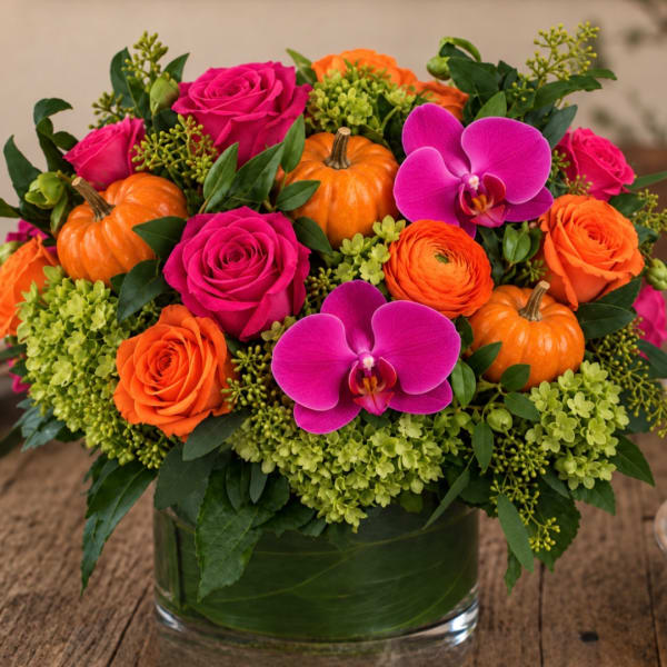 Pink and orange floral arrangement with small pumpkins in a glass vase