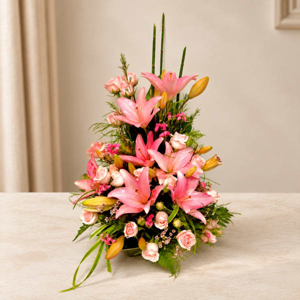 Pink lilies and roses arranged in a tall vase centerpiece