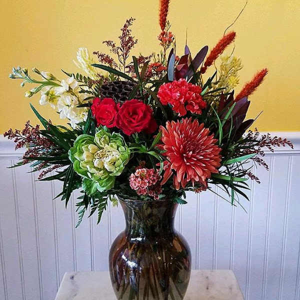 Mixed bouquet in a dark glass vase with red, white, and green blooms