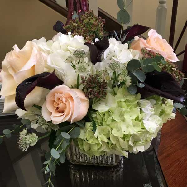 Mixed bouquet with pale roses, white hydrangeas, and dark calla lilies in a square vase