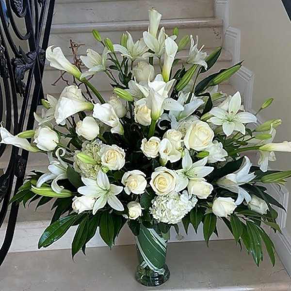 Tall white arrangement of roses, lilies, and calla lilies in a clear glass vase