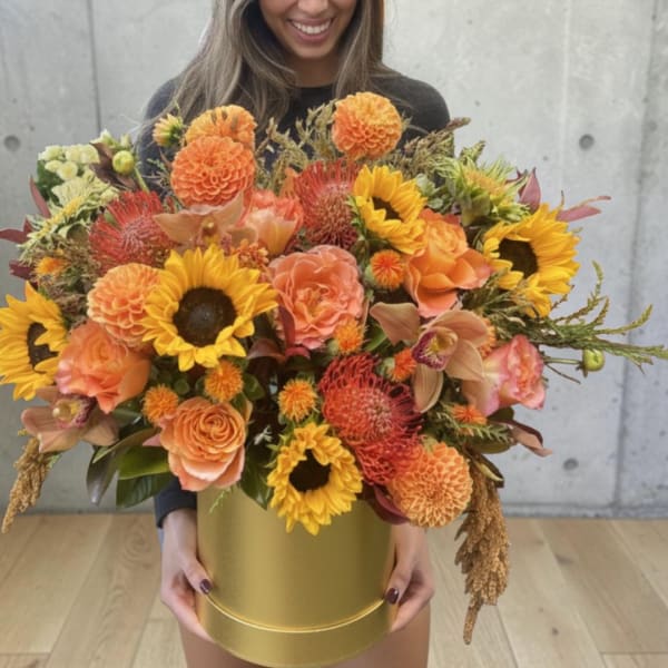 Large orange and yellow bouquet in a gold hatbox held by a woman