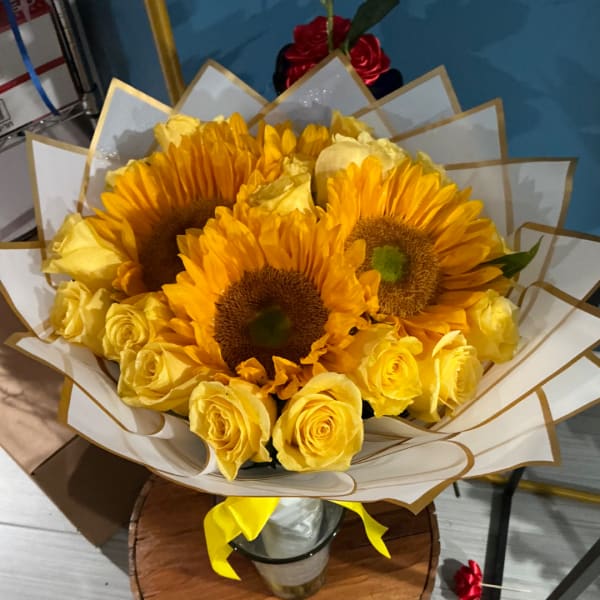 Bouquet of yellow roses and sunflowers wrapped in white paper with a yellow ribbon