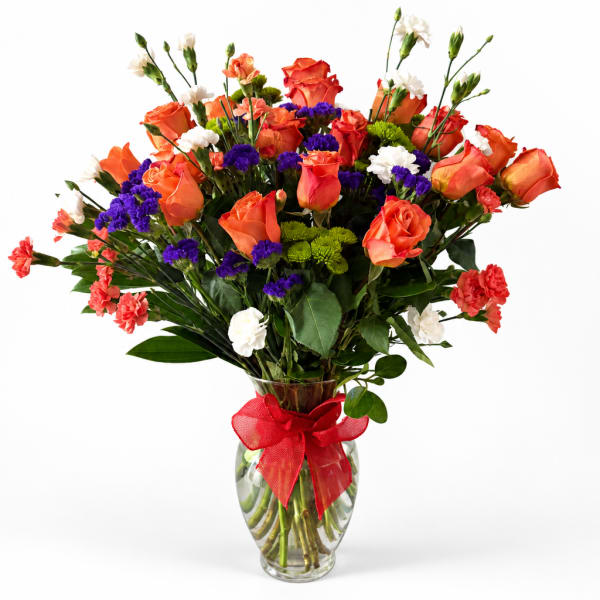 Bouquet of orange roses, purple statice, and white carnations in a glass vase