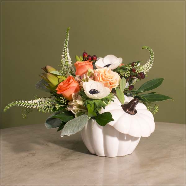 Orange roses and white anemones arranged in a white pumpkin vase