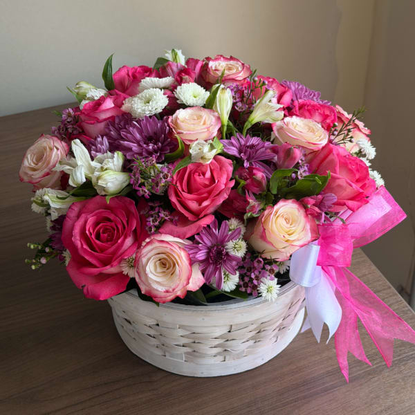 Pink and white rose bouquet in a white basket with a pink ribbon