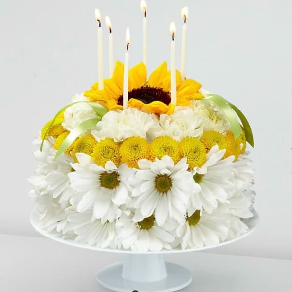 Sunflower and white daisy cake with lit candles on a pedestal stand