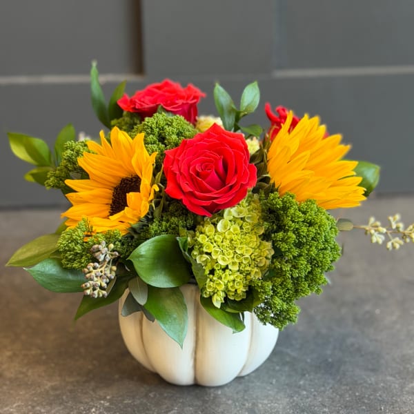 Red roses and yellow sunflowers in a white pumpkin vase