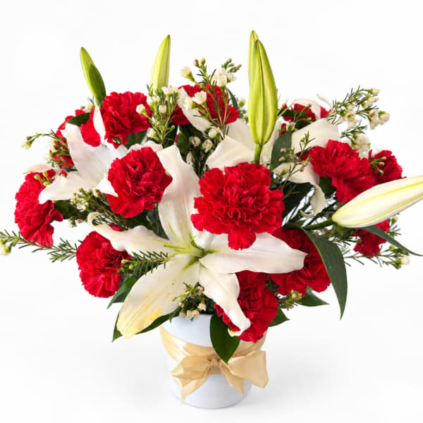 Red carnations and white lilies arranged in a white vase with a gold ribbon