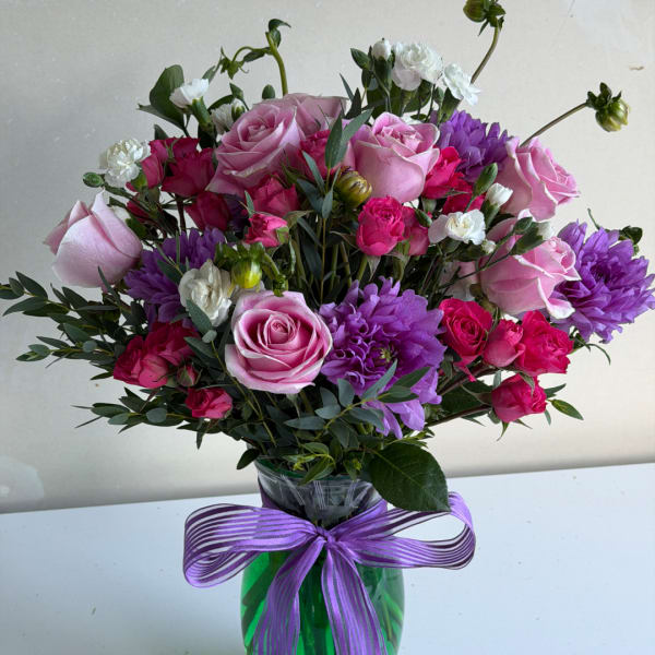 Pink and purple rose bouquet in a glass vase with a purple ribbon