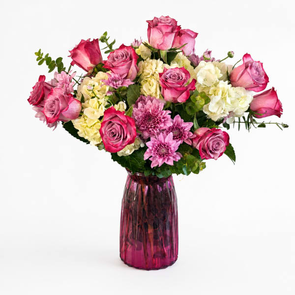 Pink and white mixed flower bouquet in a purple glass vase